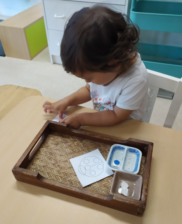 Leonnie, une petite fille de la communauté enfantine, utilise un materiel Montessori qui lui permet d'apprendre à se concentrer mais aussi à couper du papier de manière autonome.