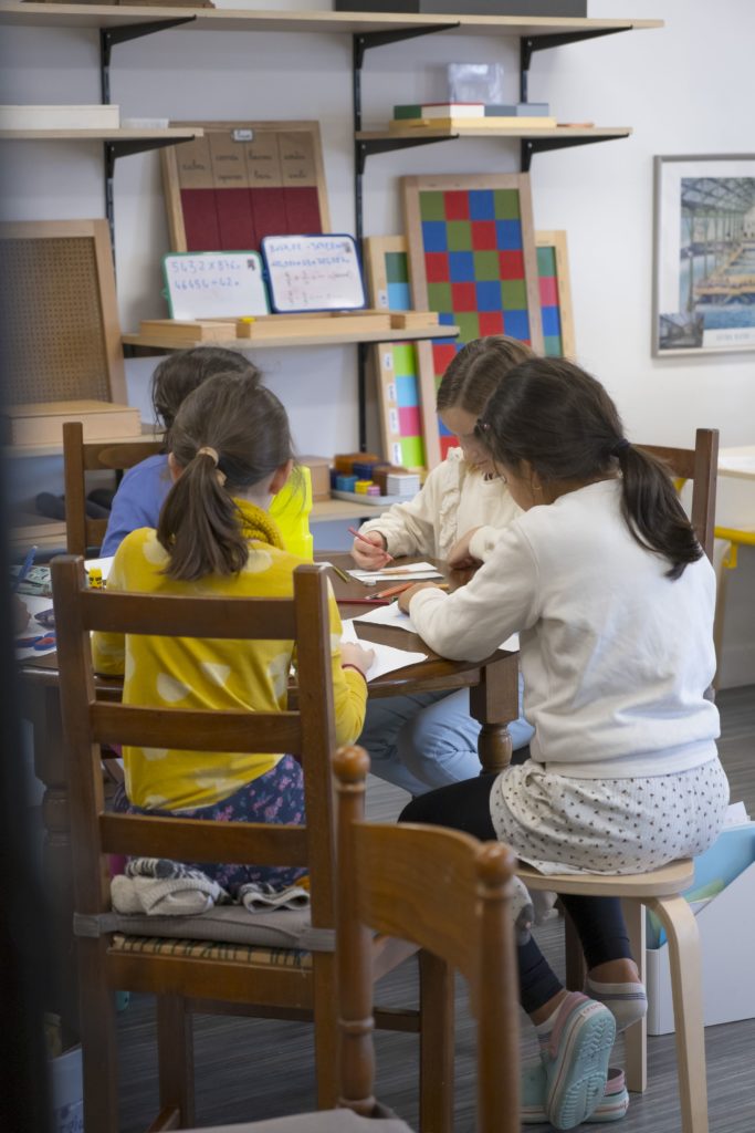 Enfant 6/12 ans assient à une table dans une ambiance Montessori. Une ambiance différente de l'education classique qui necessite un stage d'intégration