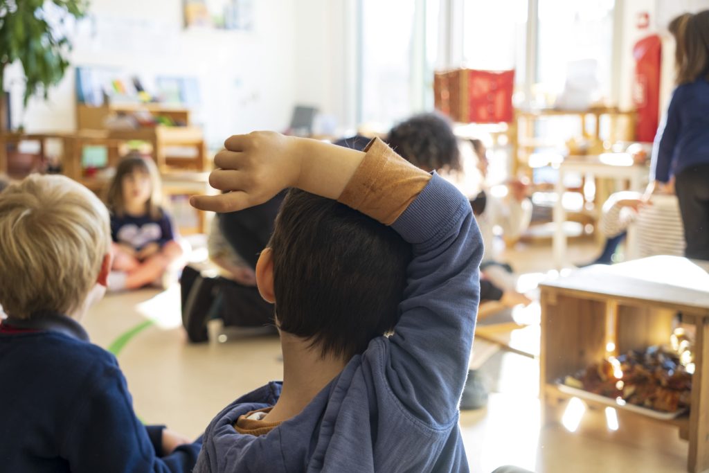 Un enfant demande de l'aide en levant la main. Dans la pédagogie Montessori il est très important de répondre présent dans ce genre de situation. C'est pourquoi ce petit garçon lève la main. Il sait qu'il aura l'attention dont il a besoin.