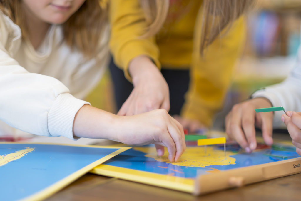 mains d'enfants faisant un travail de géographie dans une classe montessori