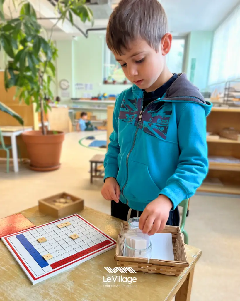 Un enfant de 5 ans utilise la table de mémorisation de l’addition dans une classe Montessori 3-6 ans, illustrant l’apprentissage sensoriel du calcul dès la maternelle.